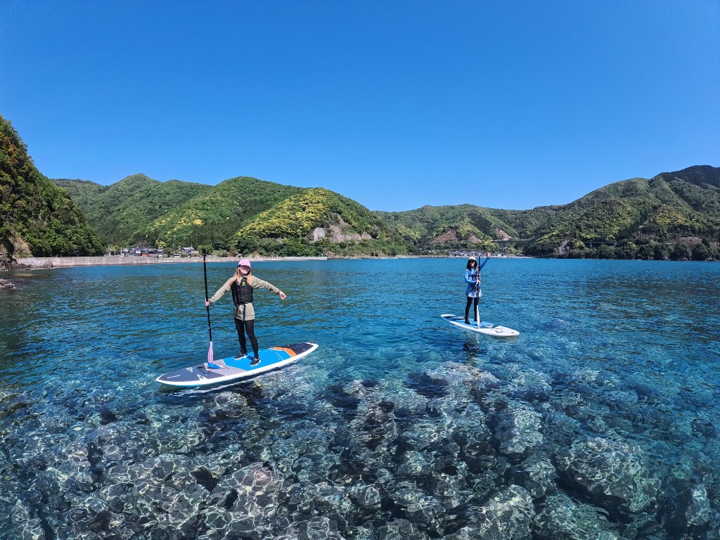 Three people paddling SUP between rocky cliffs