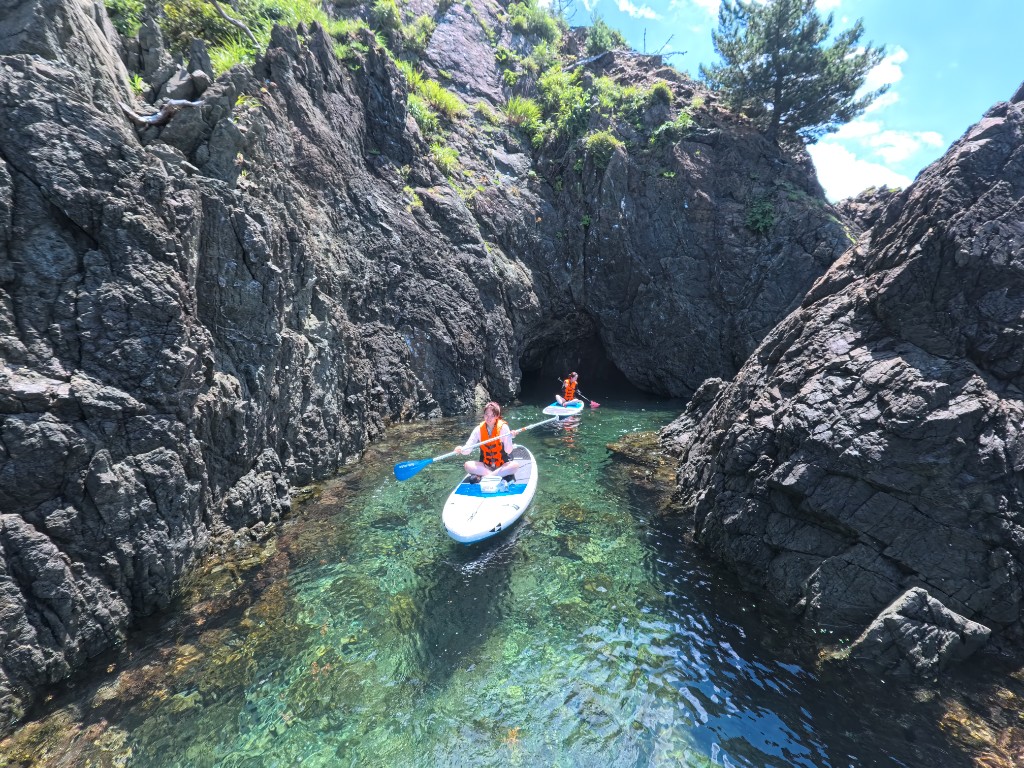 Two people paddling SUP between rocky cliffs